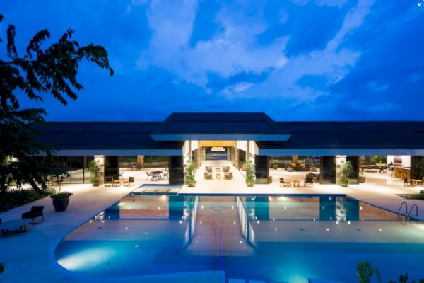 A resort at night with a large swimming pool, loungers, and an open-air pavilion, illuminated under a deep blue sky.