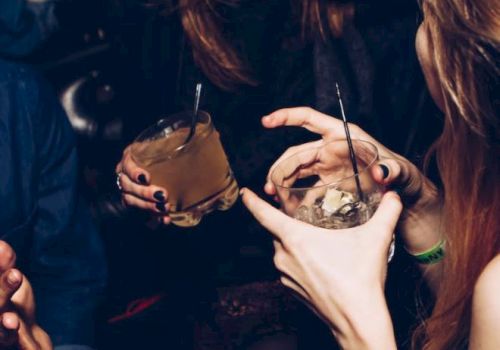 The image shows a group of people in a social setting, holding drinks, smiling, and engaging in conversation. They appear to be enjoying themselves.