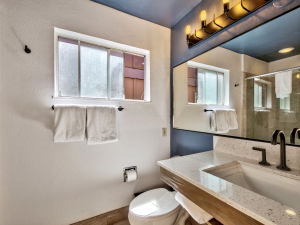 This image shows a modern bathroom with a large mirror, a vanity sink, a towel rack with two towels, a small window, and a toilet.
