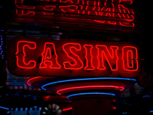 The image shows a neon sign that reads "CASINO" in bright red letters, surrounded by other colorful neon lights and reflections.
