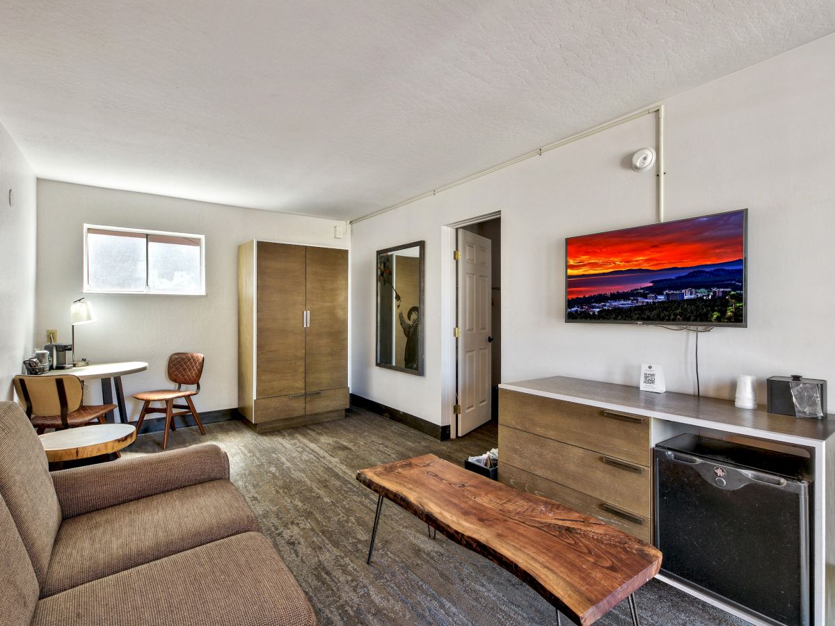 A minimalist living space featuring a couch, wooden coffee table, TV, desk, chairs, wardrobe, and a window for natural light, ending the sentence.