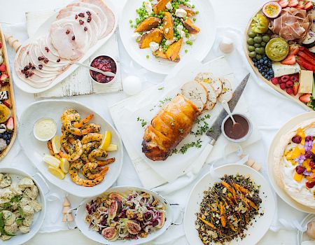 An overhead view of a festive meal with various dishes including roasted meat, shrimp, salads, fruits, vegetables, sliced meats, and desserts.