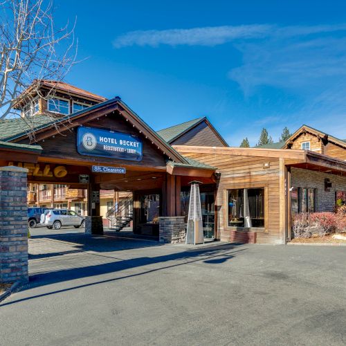 The image shows the exterior of Hotel Becket with a clear blue sky, a rustic design, and some trees nearby, suggesting a mountain setting.