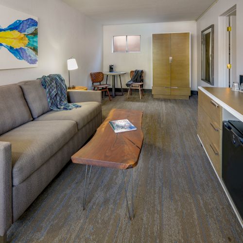 A modern living space featuring a couch, coffee table, wall art, flat-screen TV, desk, and kitchenette with a fridge and microwave ending the sentence.