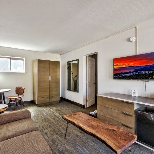 A modern living area with a brown sofa, wooden coffee table, TV, wooden cabinet, and small dining area by the window, ending the sentence.