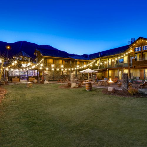 An outdoor courtyard of a building, illuminated with string lights at dusk, featuring seating areas and surrounded by hills in the background.