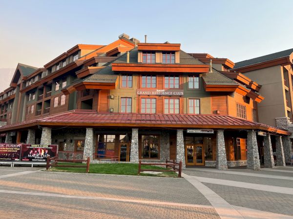 This image shows a large multi-story building with a sign reading "Grand Residences Club" and storefronts below. The architectural style is alpine lodge.