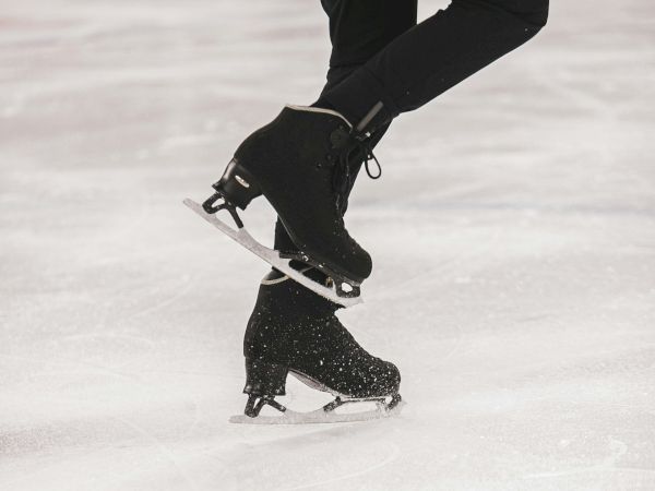 A close-up image of a figure skater's legs in black skates, captured mid-spin on an ice rink.
