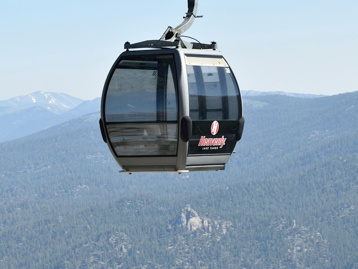 A scenic gondola lift with mountains in the background, gliding above a forested landscape on a clear day.